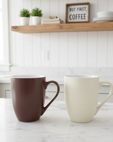 Two mugs, one brown and one white, on a cardboard surface with a blurred background.