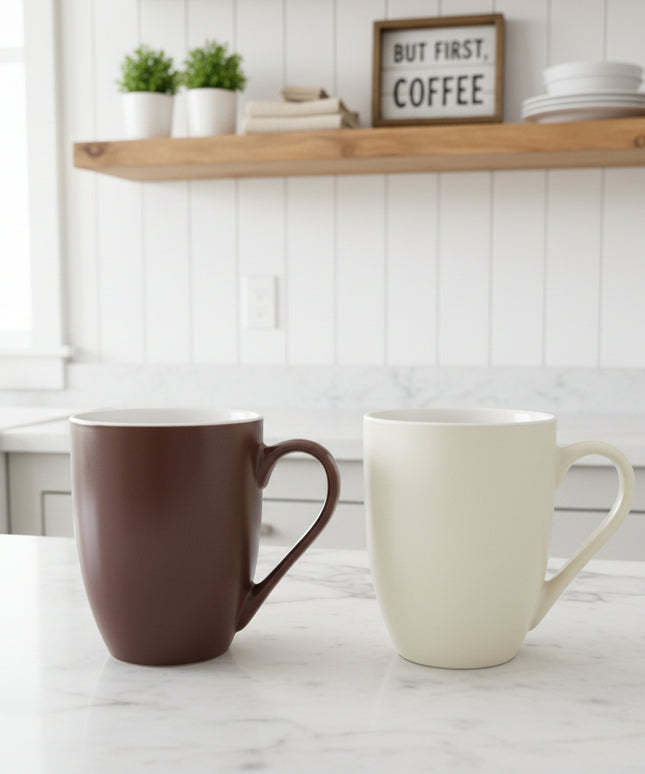 Two mugs, one brown and one white, on a cardboard surface with a blurred background.