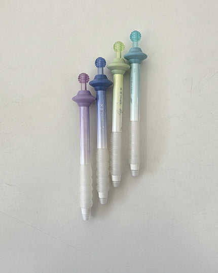 Four retractable ballpoint pens with textured translucent white barrels and colorful caps in purple, blue, light green, and teal, arranged vertically on a light gray surface.