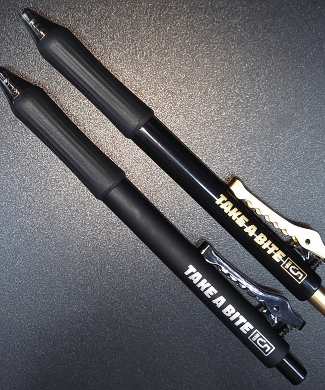 Two black pens with gold accents on a dark surface